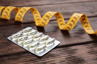 Oil capsules and measuring tape on wooden table. Weight loss