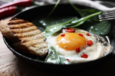 Photo of Delicious fried egg with spinach and chilli served on wooden table, closeup