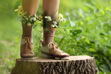 Woman standing on stump with flowers in socks outdoors, closeup