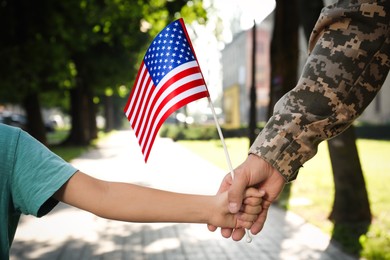 Soldier and his little son with American flag holding hands outdoors, closeup. Veterans Day in USA