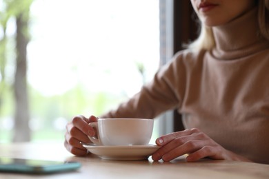 Young woman with cup of coffee at table in morning, closeup