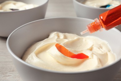 Photo of Adding orange food coloring into cream on table, closeup