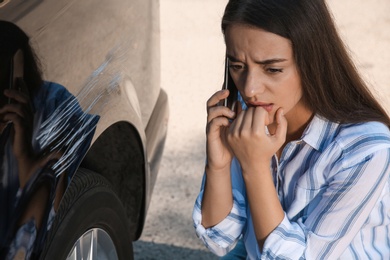 Stressed woman talking on phone near car with scratch outdoors, closeup
