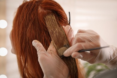 Professional hairdresser dyeing woman's hair with henna on blurred background, closeup