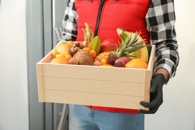 Courier holding crate with assortment of exotic fruits indoors, closeup