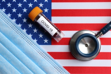 Test tube with blood sample, medical mask and stethoscope on American flag, flat lay. Coronavirus pandemic in USA