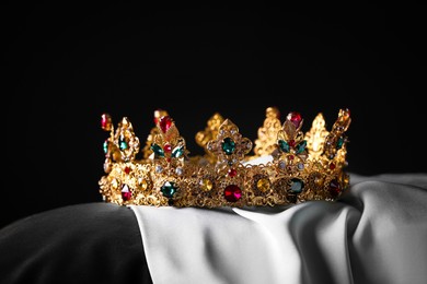 Photo of Beautiful gold crown with gems on pillow against black background