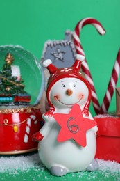 Photo of Decorative snowman with paper tag, gift box and festive decor on green background. December, 6 - Saint Nicholas Day