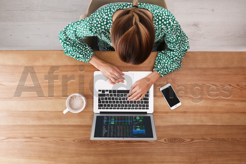 Woman analyzing electronic trading platform on laptop at wooden table, top view. Stock exchange