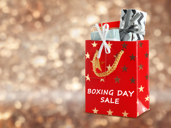 Red shopping bag with text Boxing Day Sale full of gifts on blurred gold background, closeup. Space for text