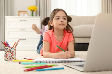 Little girl drawing on paper with pencil at online lesson indoors. Distance learning