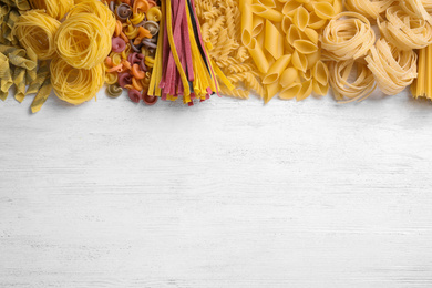 Different types of pasta on white wooden table, flat lay. Space for text
