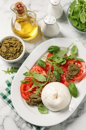 Delicious burrata salad with tomatoes, arugula and pesto sauce served on white marble table, flat lay