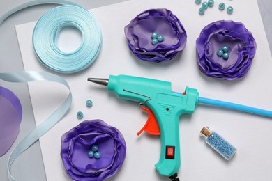 Hot glue gun, textile flowers and handicraft materials on color background, flat lay