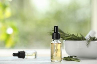 Bottle of rosemary essential oil on white wooden table against blurred background. Space for text