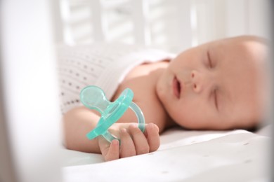 Cute little baby sleeping in crib, focus on hand with pacifier