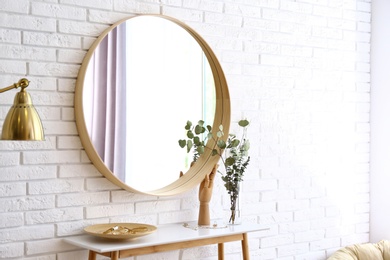Big round mirror, table with jewelry and decor near brick wall in hallway interior
