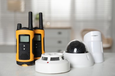 Photo of Walkie talkies, CCTV camera, smoke and movement detectors on white table indoors. Home security system