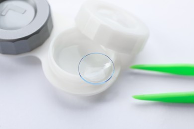Photo of Case with contact lens and tweezers on white background, closeup