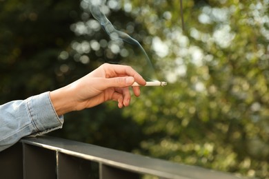 Woman smoking cigarette near railing outdoors, closeup of hand. Space for text