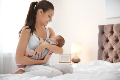Young woman with her newborn baby in bedroom. Space for text