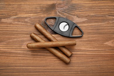 Cigars and guillotine cutter on wooden table, flat lay