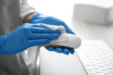 Woman in latex gloves cleaning computer mouse with wet wipe at table, closeup