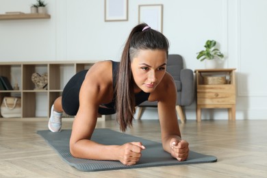 Young woman doing plank exercise on floor indoors