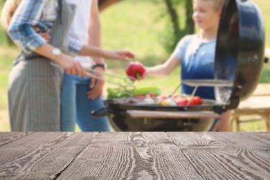 Empty wooden table and blurred view of family having barbecue with modern grill outdoors