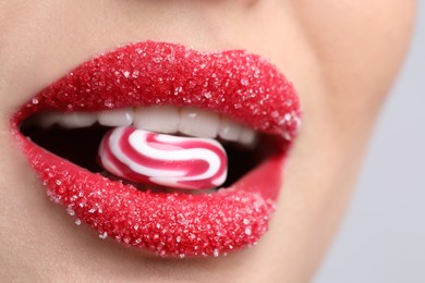 Young woman with beautiful lips covered in sugar eating candy on light background, closeup