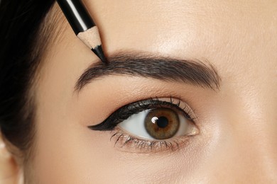 Photo of Young woman correcting eyebrow shape with pencil, closeup view