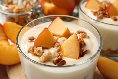 Delicious yogurt with fresh peach and granola in glass, closeup
