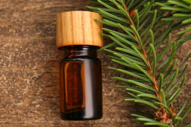 Bottle of pine essential oil and conifer tree branch on wooden table, top view