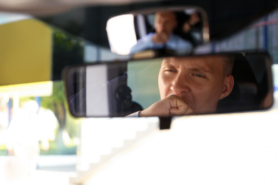 Tired young man yawning in his car, view through rear mirror