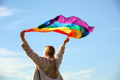 Woman holding bright LGBT flag against blue sky, back view