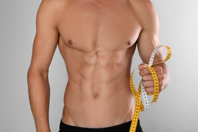 Shirtless man with slim body and measuring tape on grey background, closeup