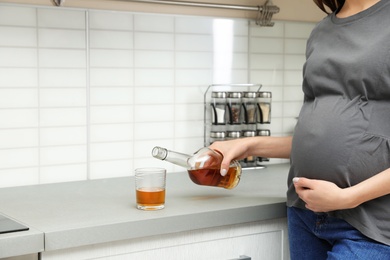 Future mother pouring alcohol drink from bottle into glass in kitchen, closeup. Bad habits during pregnancy