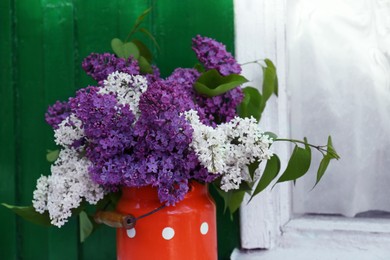 Beautiful lilac flowers in milk can near house outdoors