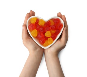 Woman holding heart shaped bowl with delicious gummy raspberry candies on white background, top view