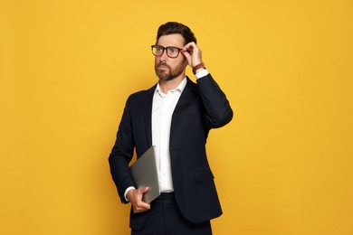 Portrait of bearded man with glasses and laptop on orange background
