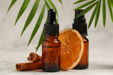 Bottles of organic cosmetic products, cinnamon sticks, dried orange slice and green leaves on light background