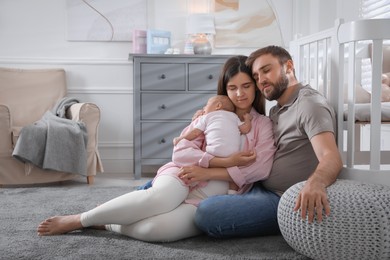 Tired young parents with their baby sleeping on floor in children's room