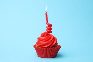 Photo of Delicious birthday cupcake with red cream and burning candle on light blue background