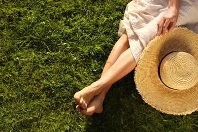 Photo of Woman with hat sitting barefoot on green grass outdoors, top view. Space for text