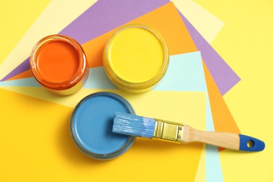 Jars of different paints and brush on color background, flat lay