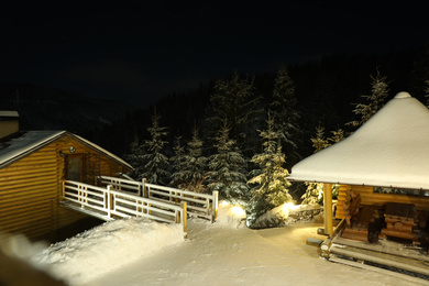 Modern cottage and wooden gazebo near snowy forest at evening