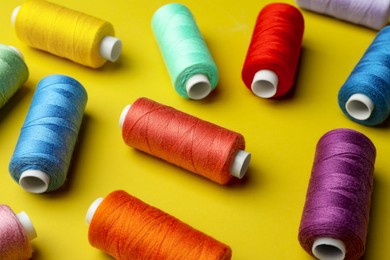 Different colorful sewing threads on yellow background