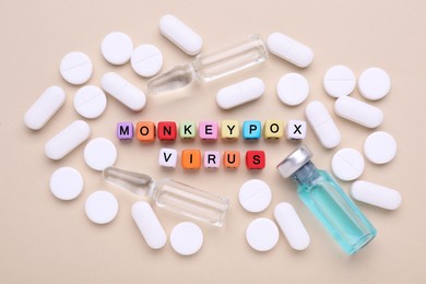 Photo of Words Monkeypox Virus made of cubes, vials and pills on beige background, flat lay