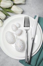 Photo of Festive table setting with painted eggs and cutlery on light grey background, flat lay. Easter celebration