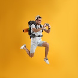 Male tourist with travel backpack taking picture on yellow background